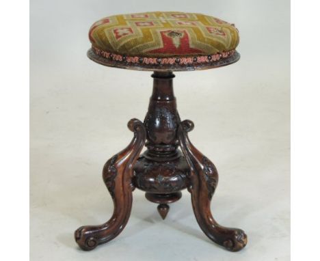 A Victorian carved walnut adjustable piano stool, having a revolving tapestry seat, on a scrolled tripod base, carved with fo