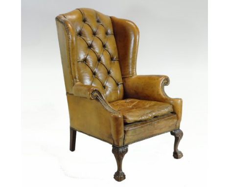 An early 20th century brown leather upholstered button back wing armchair, on claw and ball feet