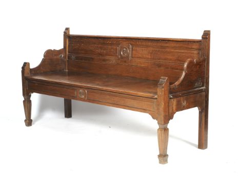 An Edwardian oak bench. With panelled back and apron, carved with roundels, on reeded tapering square legs and spade feet, L1