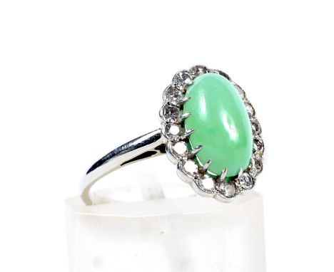 An early/mid-20th century white gold, jadeite and diamond oval cluster ring. Centred with an oval cabochon jadeite approx. 10