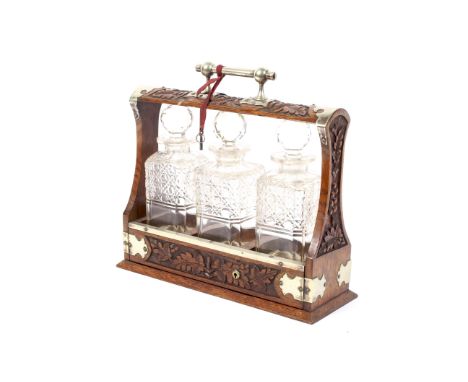 An Edwardian three-decanter brass-mounted oak tantalus. With brass handle and trefoil bracket mounts, carved with berried oak