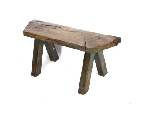 An elm pig bench of rustic shaped form with angular sides. Raised on rectangular splayed supports with signs of original pain