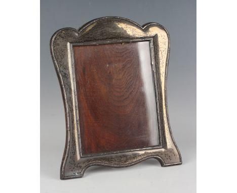 A George V silver mounted photograph frame of rectangular form with shaped outline, decorated with reeded and foliate borders