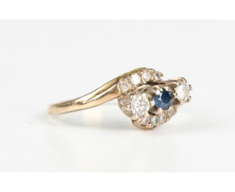 A 9ct gold, sapphire and diamond ring in a crossover design, claw set with a circular cut sapphire between the two principal 