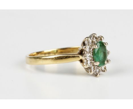 A gold, emerald and diamond oval cluster ring, claw set with the oval cut emerald within a surround of circular cut diamonds,