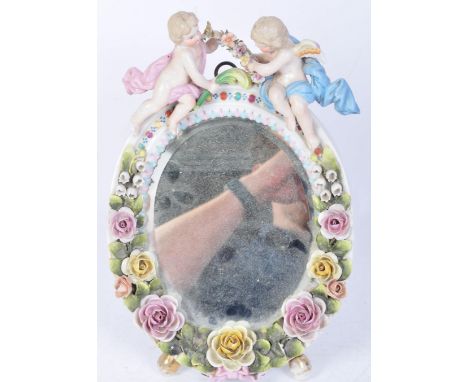 A 19th century Sitzendorf porcelain table mirror having applied decoration featuring florals and two robed putti sat atop hol