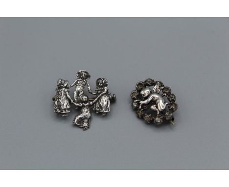 Two antique white metal brooches. Comprising a late Victorian Kate Greenaway style brooch, depicting four children in a "ring