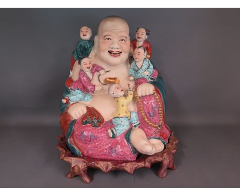 A large ceramic model of Buddha with children seated around on a carved hardwood base -  Height 32cm.
Condition Report: Good