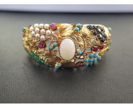 A multi-gem hinged bangle - Of openwork foliate design set with opal, rubies, turquoise, emeralds and seed pearls - Accompani