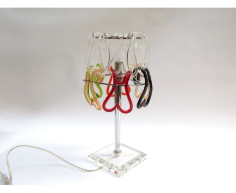 A Murano glass and stainless steel table lamp with shaped links in clear, red, orange and green glass, set on a clear glass s