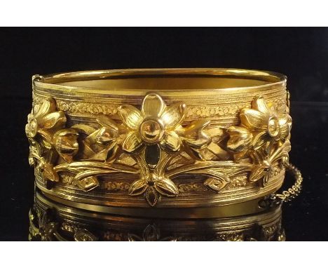 A 19th century gilt metal hinged bangle with floral decoration in high relief, 2.5 cm wide 