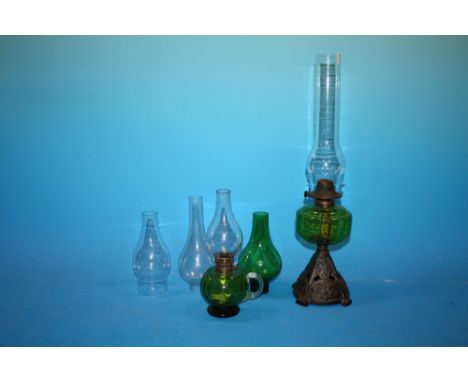 A CAST METAL AND GREEN GLASS OIL LAMP TOGETHER WITH ANOTHER AND ASSORTED LAMP FLUES