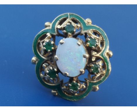 A yellow metal dress ring of open fluted oval form having green enamel decoration with six small claw set emeralds &amp; cent