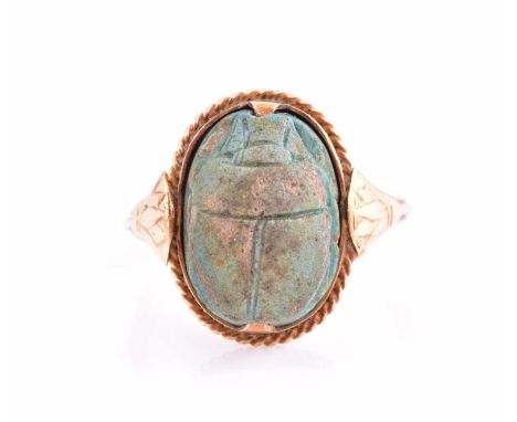An Egyptian scarab beetle ring; the antique hardstone beetle set into a ring with rope twist border and engraved shoulders an