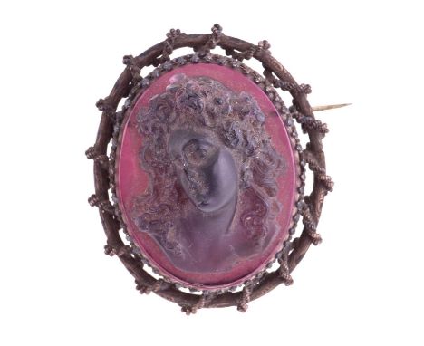  A moulded glass cameo style brooch; the purple frosted glass bust portrait of a woman with ringlets in her hair,  within a b