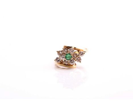 An emerald and diamond set cluster cross over ring, consisting of a central round emerald and ten-round brilliant-cut diamond