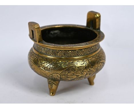 A 19th century Chinese brass tripod censer incised with dragons disputing a flaming pearl, the base with Xuande six-character