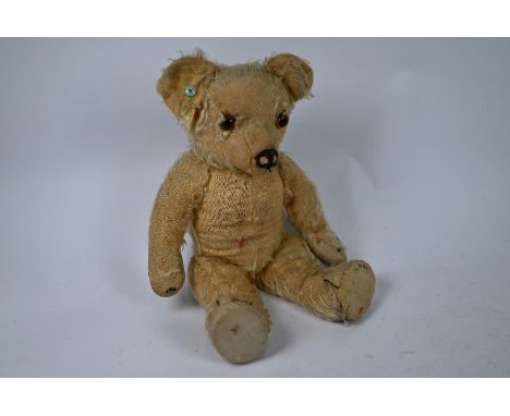 A vintage mohair teddy bear in worn condition, with turquoise ear-stud/button, glass eyes, stitched nose and claws, hump-back