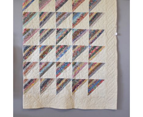 A large patchwork quilt in cream cotton-linen, having floral stitching border and central grid design, alternated with diagon