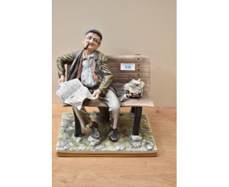 A large Capodimonte figure depicting a man on a bench smoking a pipe and reading the paper, stamped to the underneath measuri