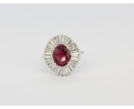 A white metal (tested high carat gold) ring set with a large oval cut ruby surrounded by tappered baguette cut diamonds, (M.5