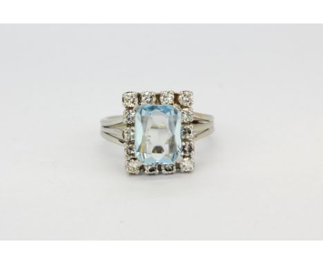 A white metal (tested high carat gold) ring set with a scissor cut aquamarine surrounded by brilliant cut diamonds, (K.5).