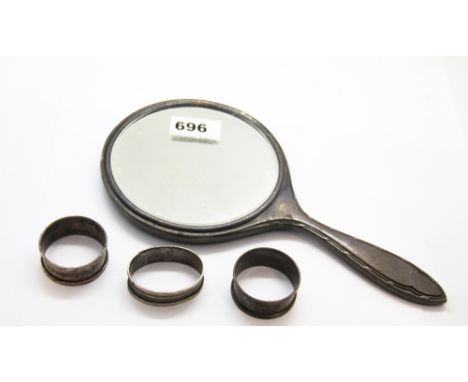 A hallmarked silver dressing mirror and three silver napkin rings.