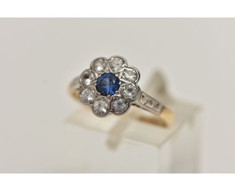 A YELLOW AND WHITE METAL CLUSTER RING, flower shape cluster set with a central circular cut sapphire in a surround of colourl