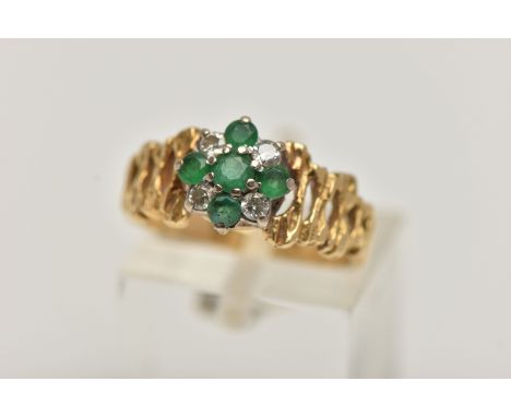 A YELLOW METAL GEM SET CLUSTER RING, flower cluster set with circular cut emeralds and diamonds, textured open work shoulders
