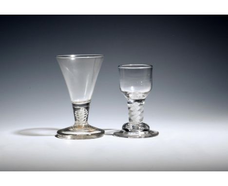 Two firing glasses  c.1765, the larger with a drawn trumpet bowl, the smaller with an ogee bowl, both raised on short opaque 