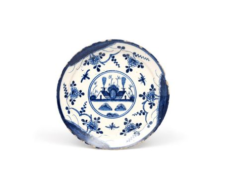 A delftware plate  c.1720-30, of pancake profile, painted in blue with a roundel containing two low buildings with smoking ch