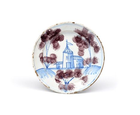A delftware 'Farmyard' plate  c.1730, probably Bristol, painted in blue with a church flanked by tall trees with sponged mang