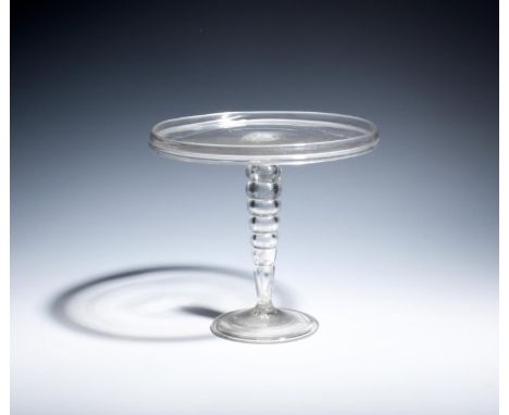 A tall glass tazza  c.1740, the flat circular top with a galleried rim, raised on a bobbin stem of six hollow knops above a f