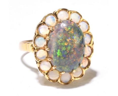 A yellow metal black opal and white opal ring, the central oval cabochon above a border of fourteen further white opals in cl