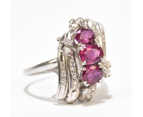 An 18ct white gold ruby and diamond ring, the three oval rubies above stepped platforms of tapering baguette and round brilli