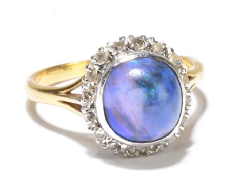 An 18ct yellow gold platinum mounted black opal and diamond set ring, the domed opal cabochon set within a border of small di