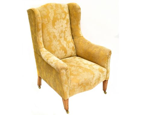 An Edwardian George III style wing armchair, with floral gold coloured upholstery, on tapered square legs with fitted brass c