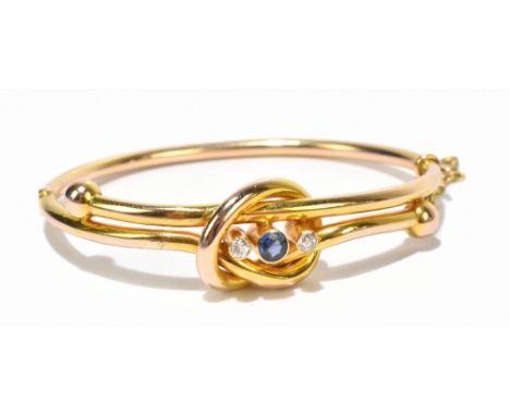 A sapphire and diamond set yellow metal bangle, formed as a knot with a central sapphire flanked by two diamonds, with guard 