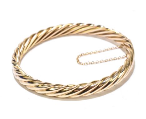 A 9ct yellow gold hinged snap bangle of wrythen moulded form with integral 9ct white gold adjustable bar and with safety chai