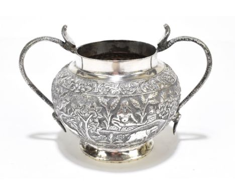 An Indian white metal twin handled sugar bowl with rising snake head handles and decorated with figures and animals in a cont