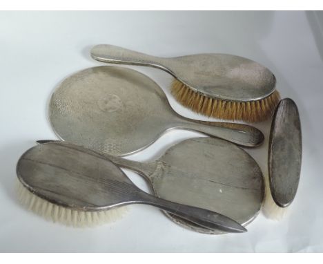 Five HM silver backed hand mirrors and brushes having engine turned decoration, AF