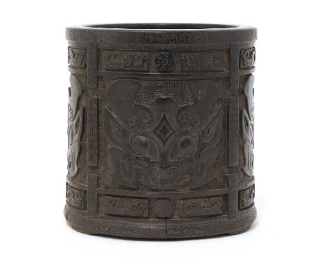 A Chinese wood brush pot,of cylindrical form on three bracket feet, carved with taotie masks against a key fret diapered grou