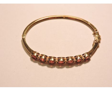 A hinged gold bangle, set with a row of garnets tested as approximately 9ct gold