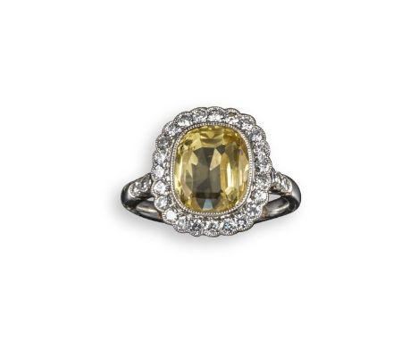 A yellow sapphire and diamond cluster ring, the cushion-shaped yellow sapphire is millegrain-set within a surround of circula