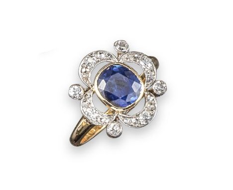 A sapphire and diamond cluster ring, the cushion-shaped sapphire is set within a scallop-edged border of circular-cut diamond