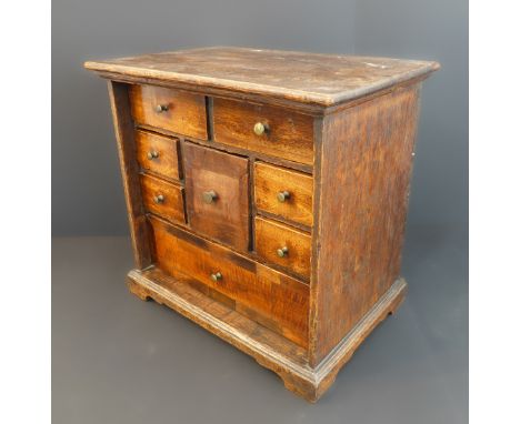 An antique oak miniature table cabinet with drawers: eight varying sized drawers and raised on bracket feet (35.5 cm wide x 2