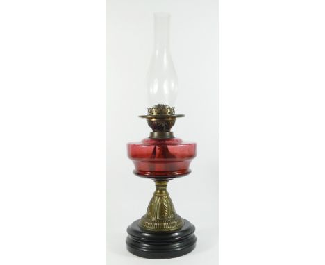 Victorian brass oil lamp with cranberry glass globe, raised on a ceramic base - 58cm tall. 