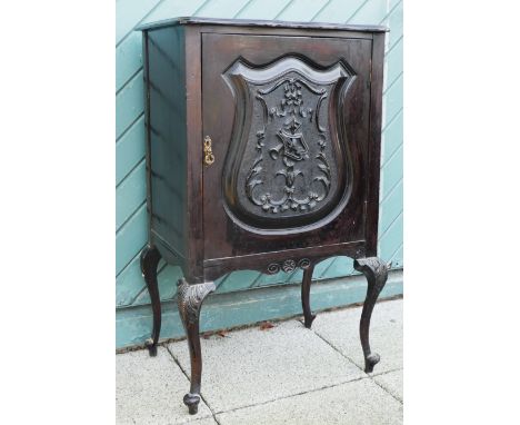 A French Louis XIV style ebonised music cabinet having scalloped edge top above a carved panel door, raised on cabriole legs 