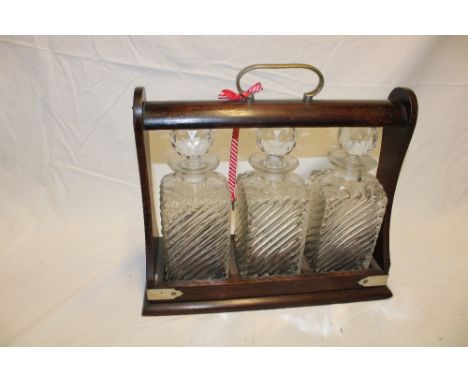 A three bottle tantalus with moulded glass decanters (one with slight damage) in oak tantalus with electroplated mounts