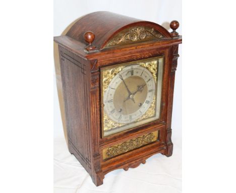 A German bracket clock with gilt and silvered square dial in carved oak and  brass mounted arched case 15" high